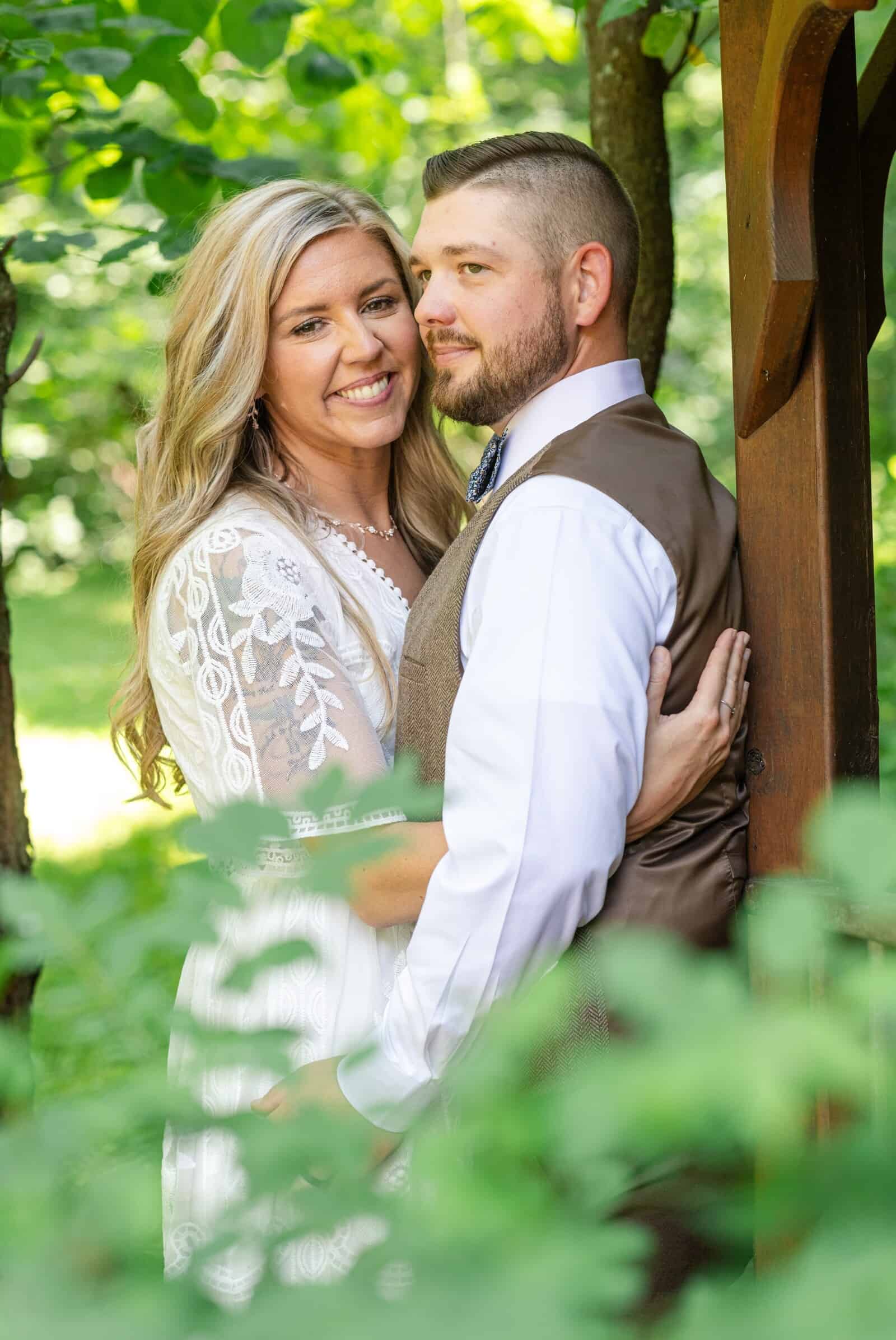 bride and groom hug next to a gazebo under the trees